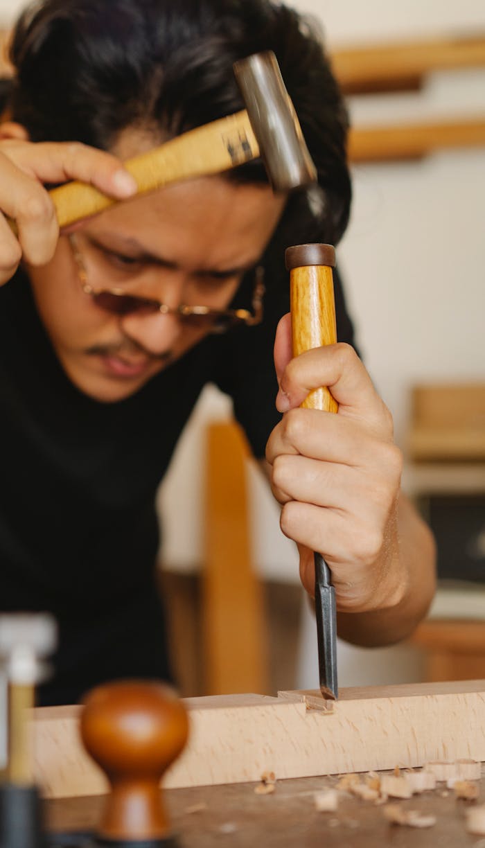Crafting Captivating Headlines: Your awesome post title goes here Attentive young ethnic male master in eyeglasses carving wooden plank with chisel and hammer in traditional workshop