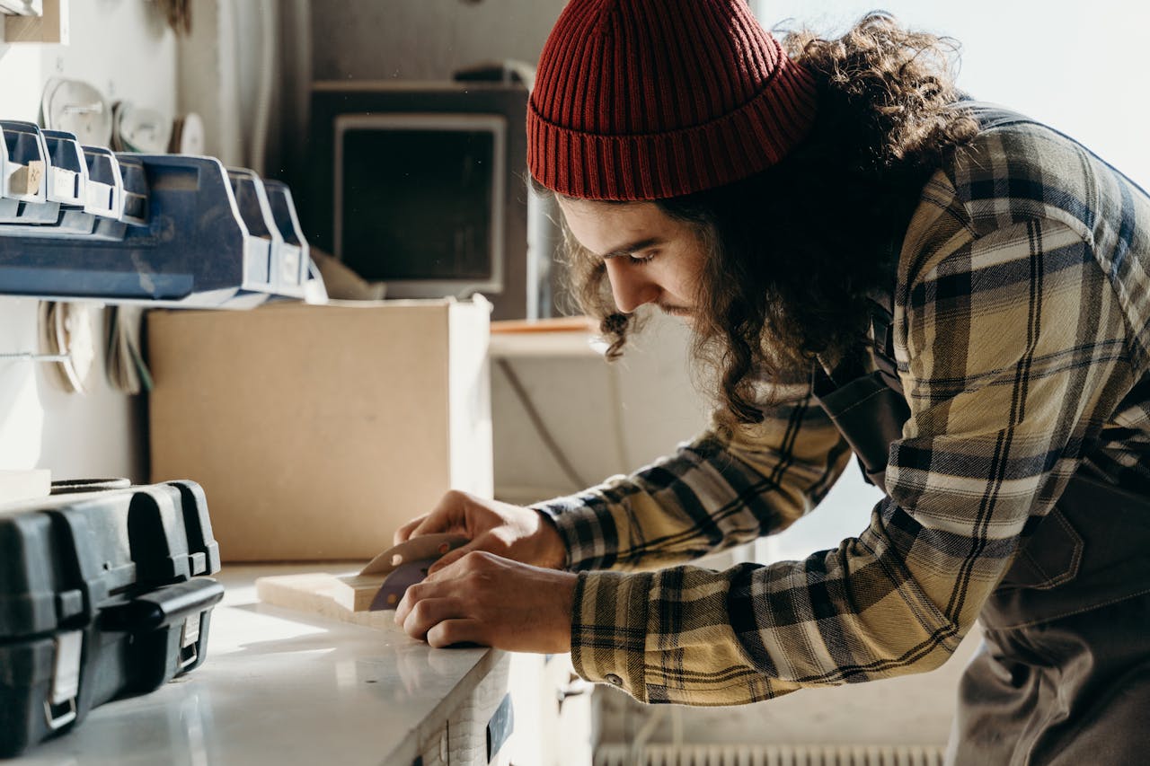 about-us Focused young male carpenter sanding wood at a workbench indoors.